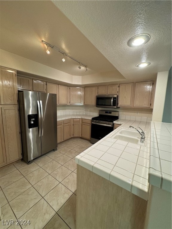 kitchen with tile counters, kitchen peninsula, sink, and stainless steel appliances