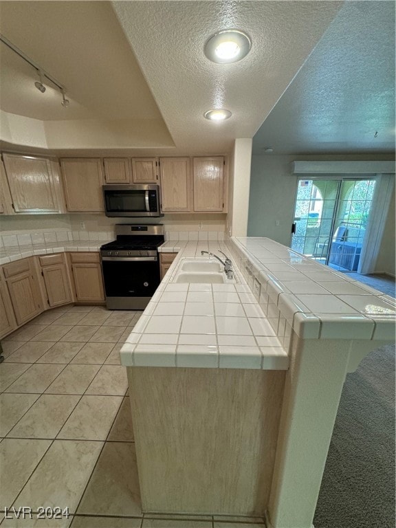 kitchen featuring kitchen peninsula, stainless steel appliances, tile countertops, light brown cabinetry, and sink