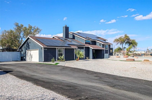view of front of property featuring solar panels, a chimney, an attached garage, driveway, and fence