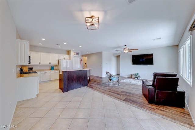 kitchen with light hardwood / wood-style floors, an island with sink, white cabinets, white fridge, and ceiling fan