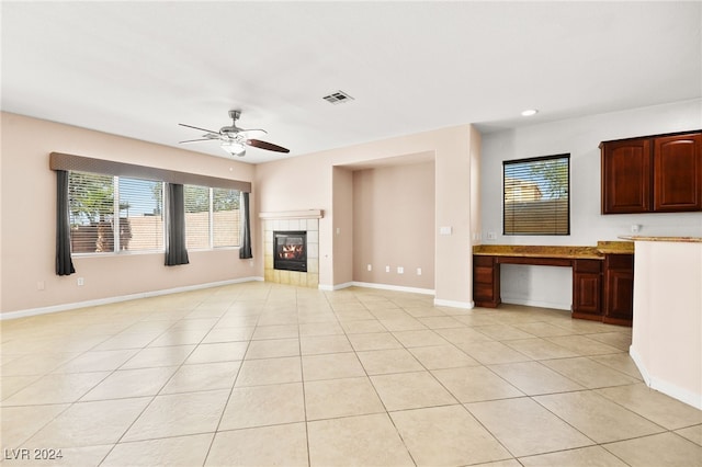 unfurnished living room with ceiling fan, light tile patterned flooring, and a tiled fireplace