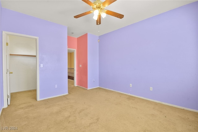 unfurnished bedroom with light carpet, ceiling fan, and a walk in closet