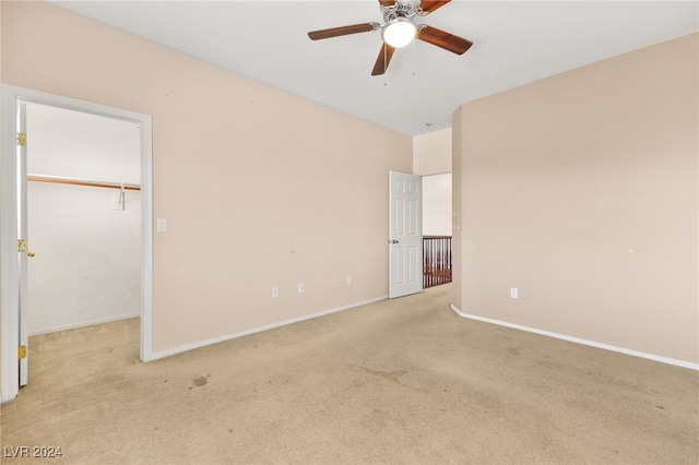 interior space with light carpet, a closet, ceiling fan, and a walk in closet