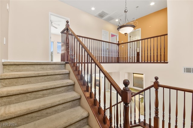 stairs featuring ceiling fan with notable chandelier and a towering ceiling