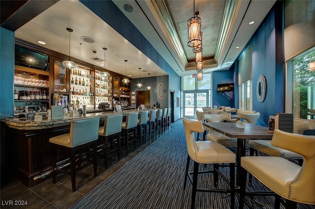 dining area featuring a healthy amount of sunlight, a raised ceiling, dark tile patterned floors, and indoor bar