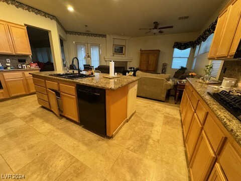 kitchen with light stone countertops, black appliances, a center island, ceiling fan, and sink