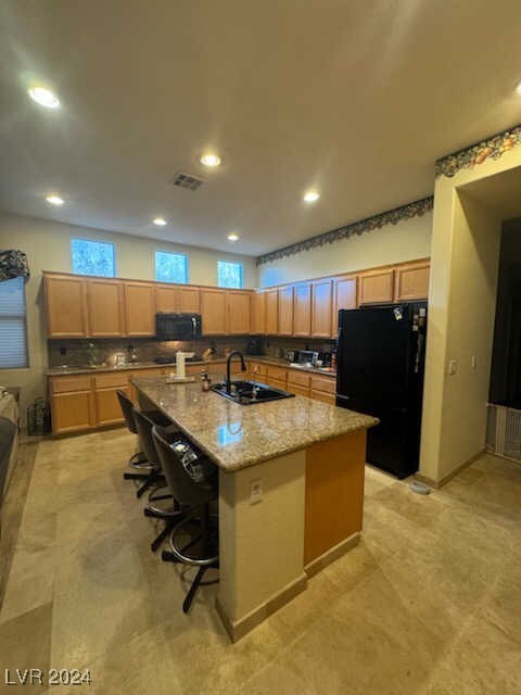 kitchen featuring light stone counters, sink, an island with sink, a kitchen bar, and black appliances