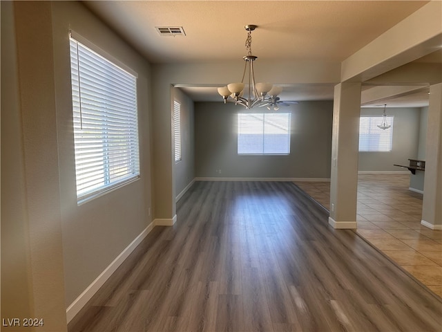 unfurnished dining area with a notable chandelier, plenty of natural light, and dark hardwood / wood-style flooring