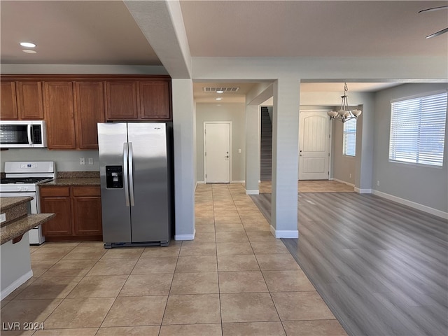 kitchen with appliances with stainless steel finishes, light wood-type flooring, an inviting chandelier, and decorative light fixtures