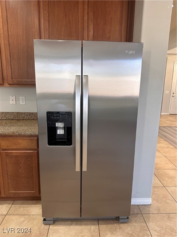 kitchen with stone counters, light tile patterned flooring, and stainless steel fridge