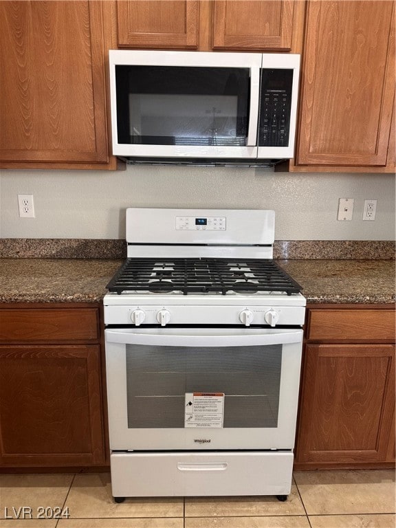 kitchen featuring dark stone counters, white gas range oven, and light tile patterned flooring