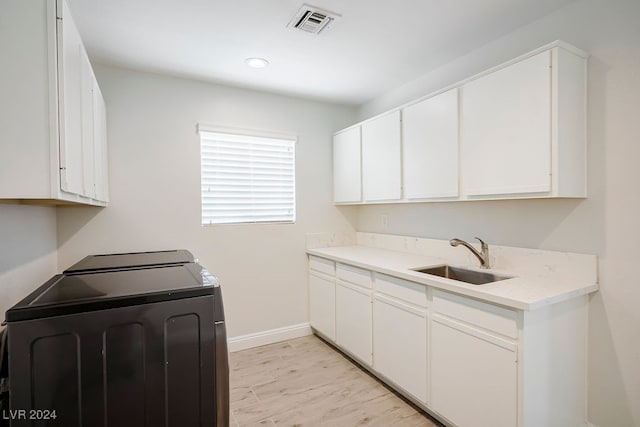 laundry room featuring washing machine and dryer, sink, cabinets, and light wood-type flooring