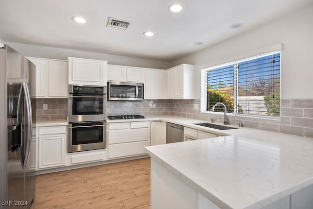 kitchen with kitchen peninsula, stainless steel appliances, sink, white cabinets, and light hardwood / wood-style floors