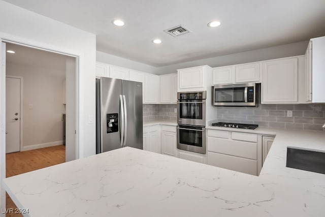 kitchen featuring white cabinets, light stone countertops, stainless steel appliances, and tasteful backsplash