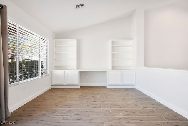 spare room featuring light wood-type flooring, lofted ceiling, and built in desk