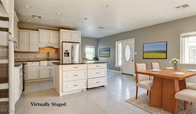 kitchen with light tile patterned floors, sink, a center island, and stainless steel fridge