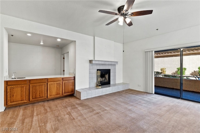 unfurnished living room with a tiled fireplace, sink, ceiling fan, and light colored carpet