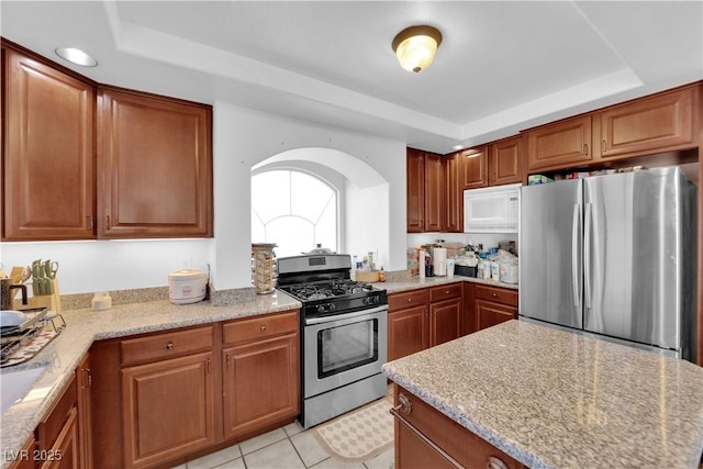 kitchen featuring a tray ceiling, brown cabinetry, light stone countertops, and appliances with stainless steel finishes