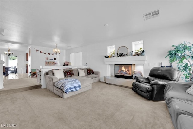 carpeted living room with visible vents, an inviting chandelier, and a glass covered fireplace