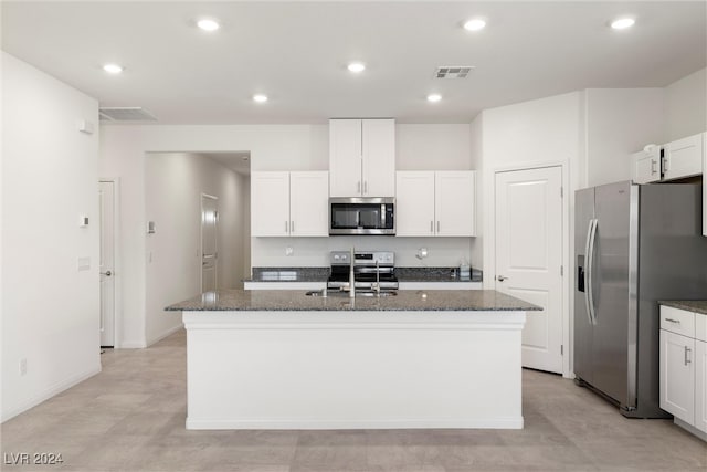 kitchen featuring appliances with stainless steel finishes, dark stone counters, a center island with sink, and white cabinets