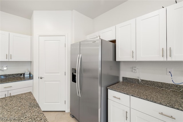 kitchen with white cabinetry, dark stone countertops, light tile patterned flooring, and stainless steel fridge