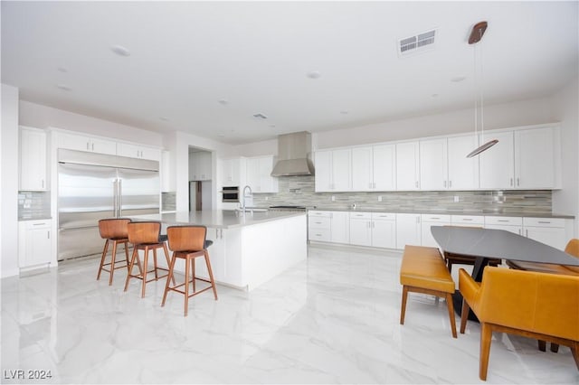 kitchen featuring stainless steel appliances, white cabinets, a center island with sink, and wall chimney range hood