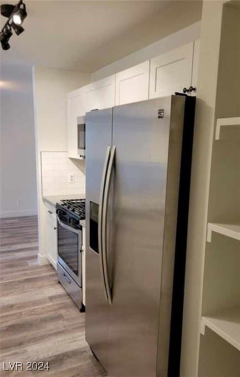 kitchen with appliances with stainless steel finishes, light hardwood / wood-style floors, tasteful backsplash, and white cabinetry