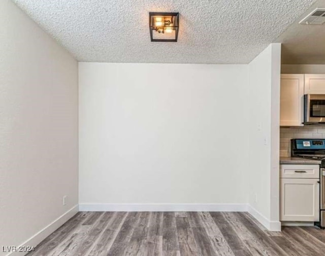 unfurnished dining area featuring a textured ceiling and light hardwood / wood-style floors