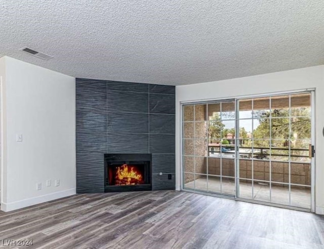 unfurnished living room featuring wood-type flooring, a textured ceiling, and a tiled fireplace