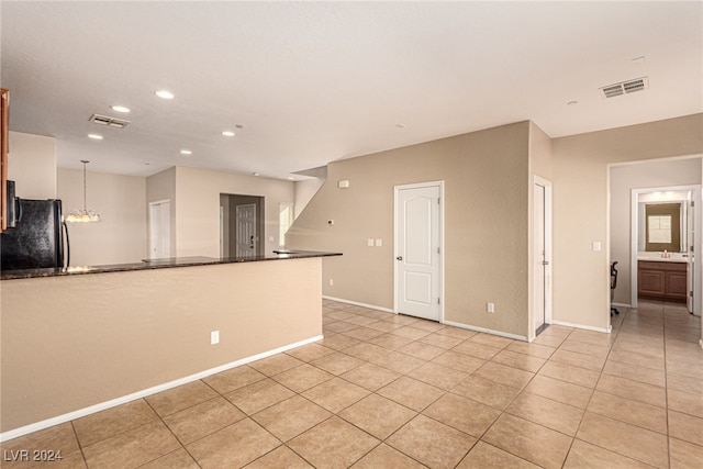 kitchen featuring black refrigerator, light tile patterned flooring, and decorative light fixtures