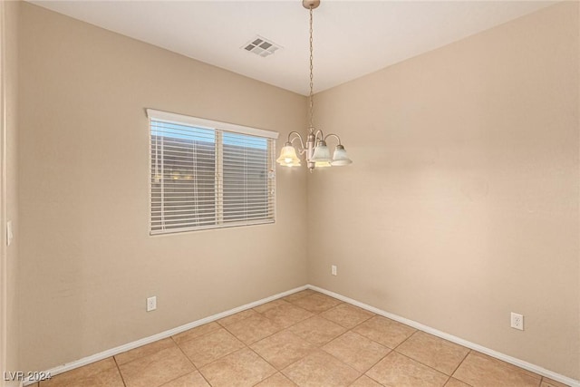 tiled spare room with a notable chandelier