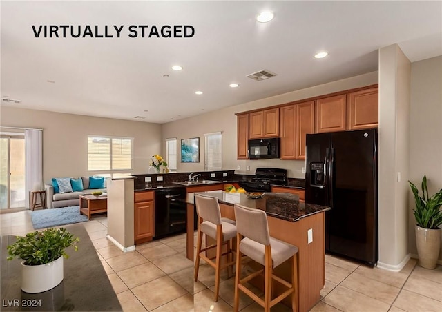 kitchen featuring a kitchen bar, kitchen peninsula, black appliances, dark stone countertops, and a center island