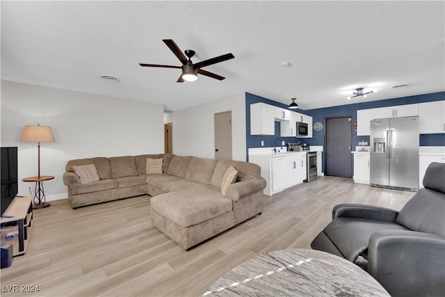 living room featuring sink, a textured ceiling, light hardwood / wood-style floors, and ceiling fan