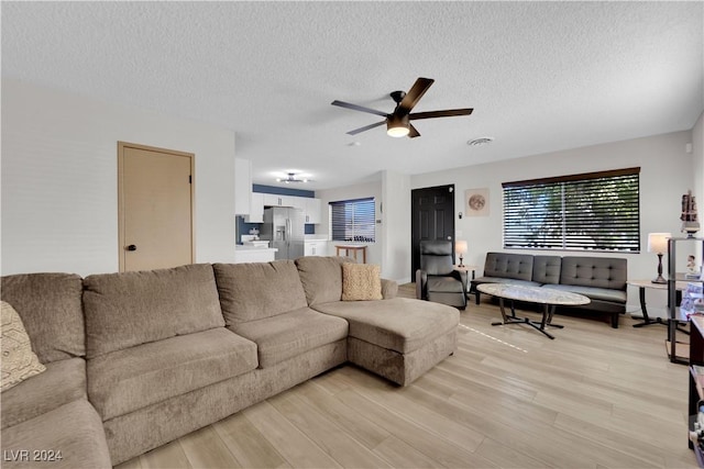 living room with ceiling fan, a textured ceiling, and light hardwood / wood-style floors