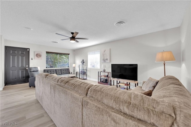 living room featuring ceiling fan, light hardwood / wood-style flooring, and a textured ceiling