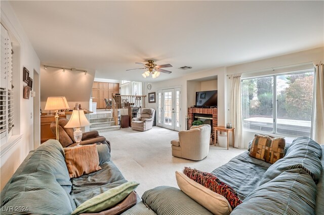 carpeted living room featuring ceiling fan, a brick fireplace, plenty of natural light, and french doors