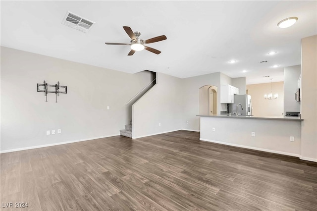 unfurnished living room featuring ceiling fan with notable chandelier, dark wood-type flooring, and sink