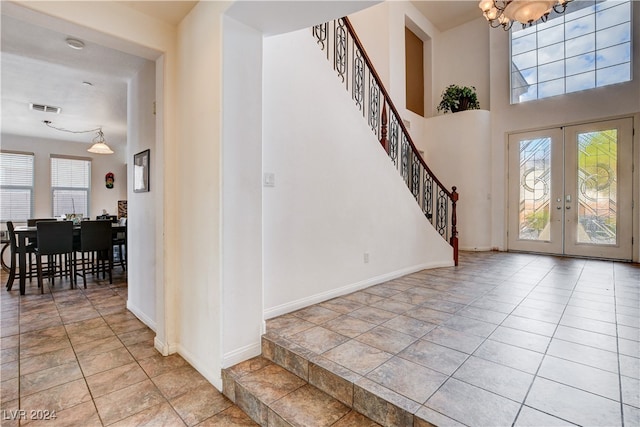 tiled entrance foyer with an inviting chandelier, a high ceiling, plenty of natural light, and french doors