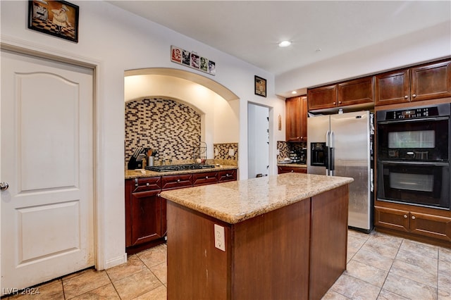 kitchen with appliances with stainless steel finishes, decorative backsplash, light tile patterned flooring, light stone countertops, and a center island