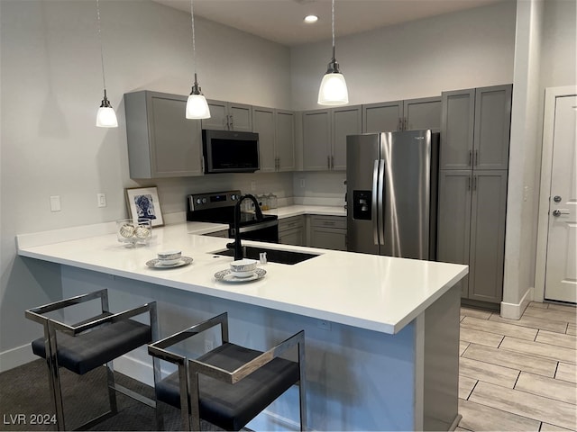 kitchen with pendant lighting, kitchen peninsula, gray cabinets, stainless steel appliances, and a breakfast bar