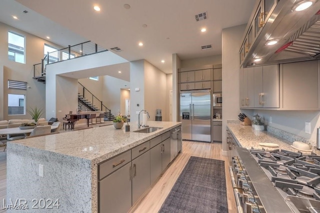 kitchen featuring a kitchen island with sink, sink, ventilation hood, stainless steel appliances, and a high ceiling