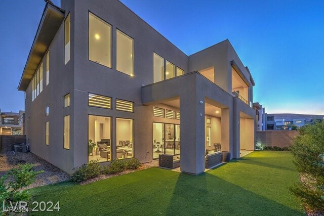 back house at dusk featuring a lawn, a patio area, and central air condition unit