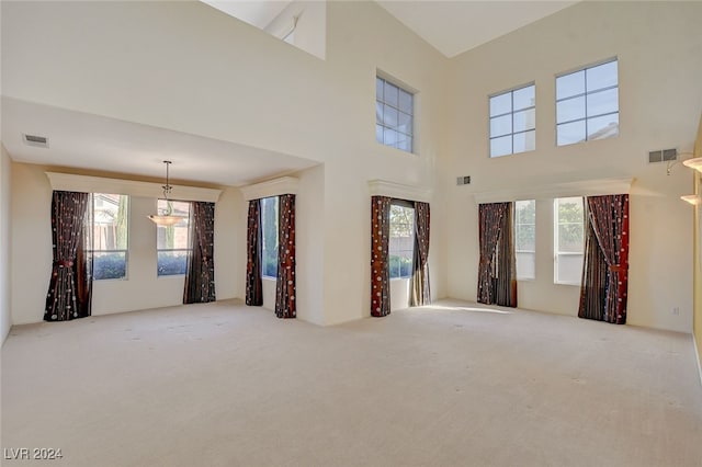 carpeted empty room featuring a towering ceiling and a healthy amount of sunlight