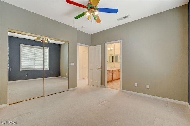 unfurnished bedroom featuring ceiling fan, a closet, light carpet, and ensuite bath