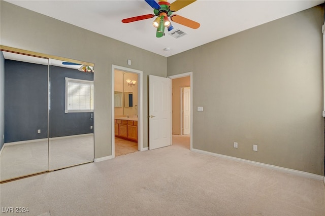 unfurnished bedroom featuring a closet, connected bathroom, light colored carpet, and ceiling fan