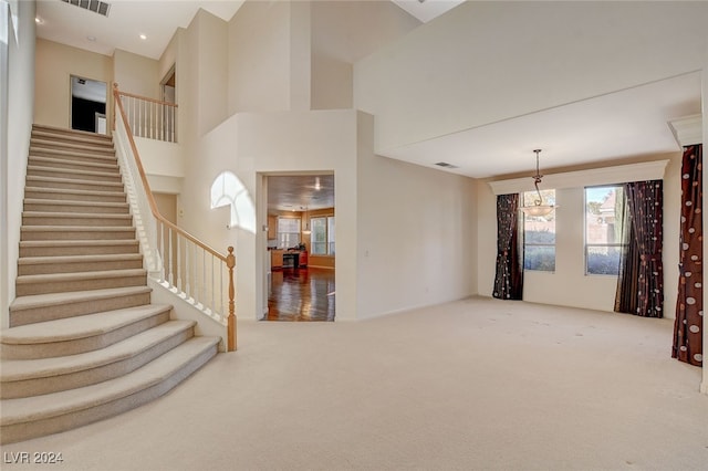 unfurnished living room featuring carpet flooring, a high ceiling, and an inviting chandelier