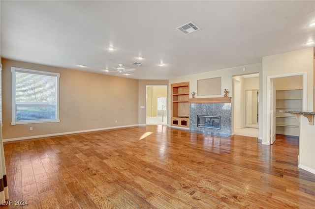 unfurnished living room with a fireplace, built in shelves, light hardwood / wood-style flooring, and ceiling fan