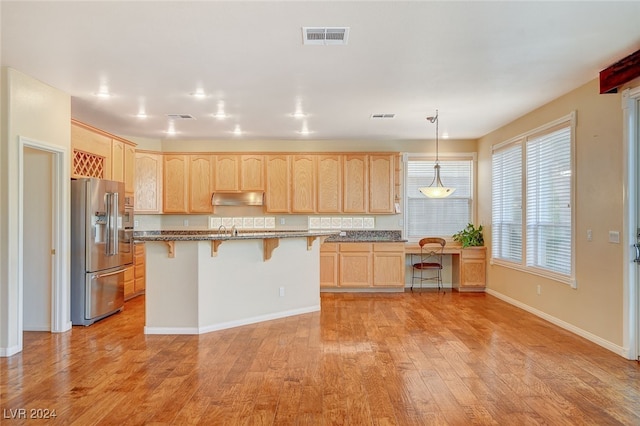 kitchen featuring light brown cabinetry, high quality fridge, decorative light fixtures, light hardwood / wood-style flooring, and a kitchen island