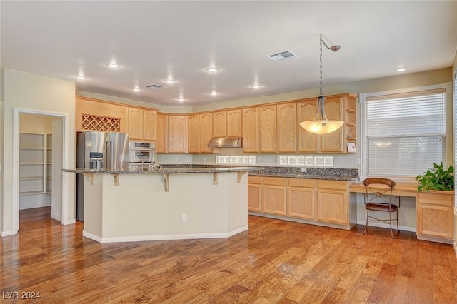 kitchen with stainless steel appliances, hanging light fixtures, a breakfast bar, a kitchen island, and light wood-type flooring