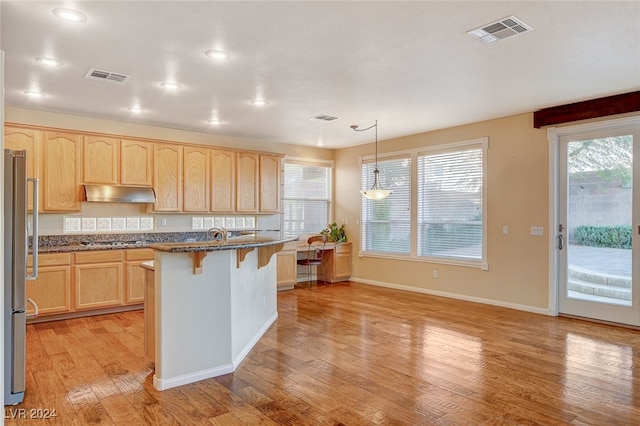 kitchen featuring light brown cabinetry, light wood-type flooring, decorative light fixtures, a center island, and a breakfast bar area